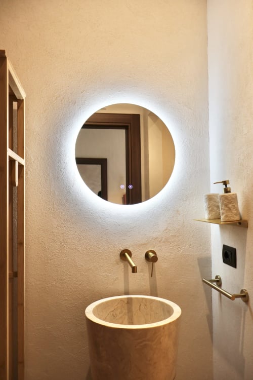 Bagno moderno a Tagasuites Catania con specchio circolare illuminato, lavabo in legno e rubinetteria in ottone nell'appartamento 107
