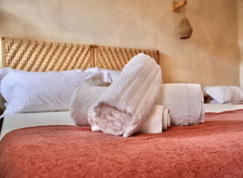 Asciugamani bianchi e beige arrotolati su un letto in terracotta all'appartamento Tagasuites di Catania
