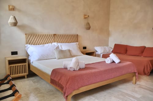Camera da letto moderna a Tagasuites Catania con letto in legno, biancheria bianca, plaid corallo, lampade a sospensione e zona living