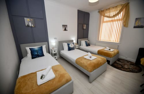 Modern triple bedroom at Love Short Stays with white beds, mustard throws, navy headboard, and large window with striped