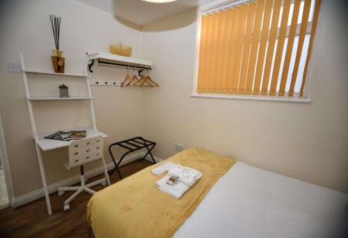 Modern bedroom at Love Short Stays with yellow bedding, desk, ladder shelving, and vertical blinds with garden view