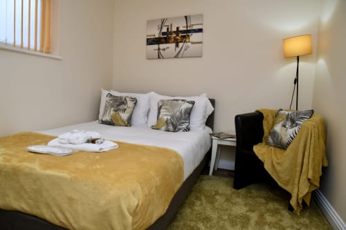 Cozy hotel bedroom at Love Short Stays with gold velvet bedding, white linens, decorative pillows, and modern lamp in South