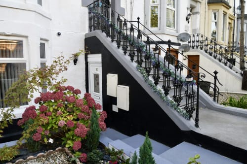 Garden view entrance of Love Short Stays apartment with pink flowers, black railings and modern exterior in South Shields