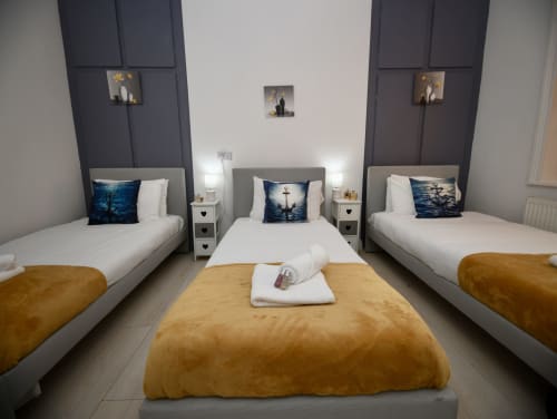 The Lower Deck triple bedroom at Love Short Stays featuring three beds with nautical-themed pillows and gold throws, modern