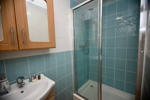 Modern bathroom with teal tile walls, glass shower enclosure, white sink and wooden vanity at Love Short Stays hotel