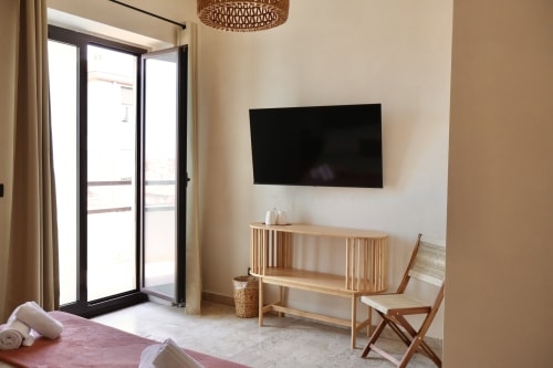 Suite Deluxe moderna presso Tagasuites Catania con TV a parete, mobili in legno e accesso al balcone con vista sulla città