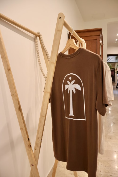 Maglietta marrone con stampa di palme appesa a uno stendipanni in legno presso Tagasuites, Catania