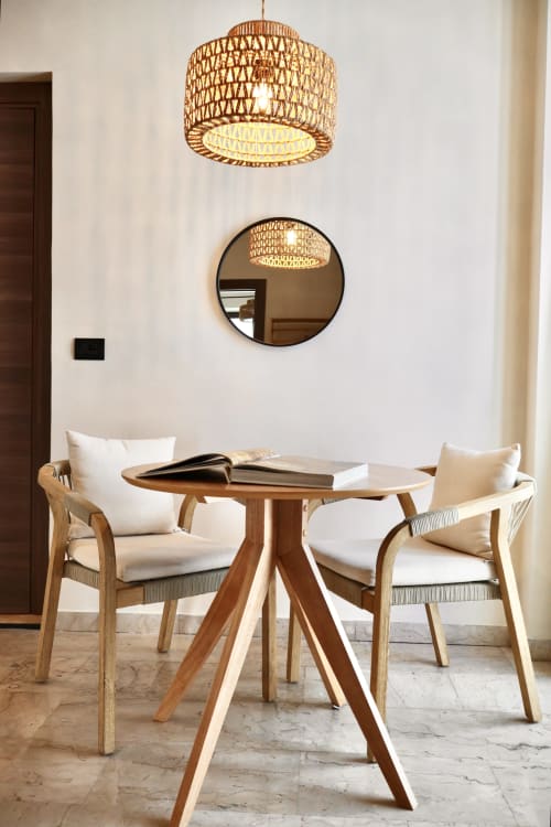 Zona living moderna nella suite Tagasuites Catania con tavolo in legno, sedie imbottite, lampada sospesa intrecciata e specchio tondo