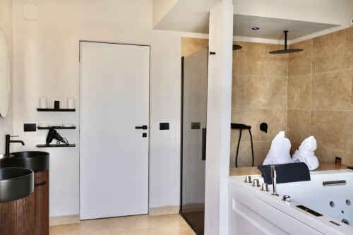 Modern bathroom at Tagasuites Catania with black circular sink, white door, tan tile shower with rainfall showerhead, and