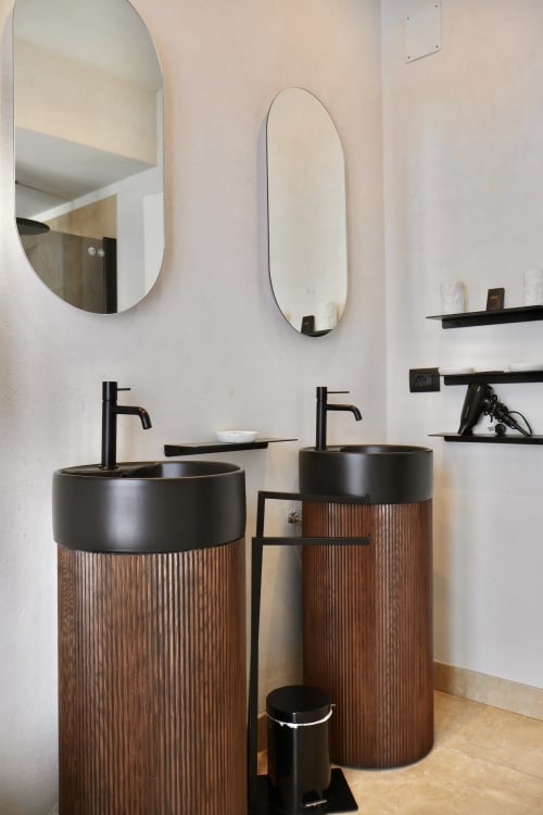 Modern bathroom vanity with dual black vessel sinks, wooden pedestal bases, and oval mirrors at Tagasuites Catania
