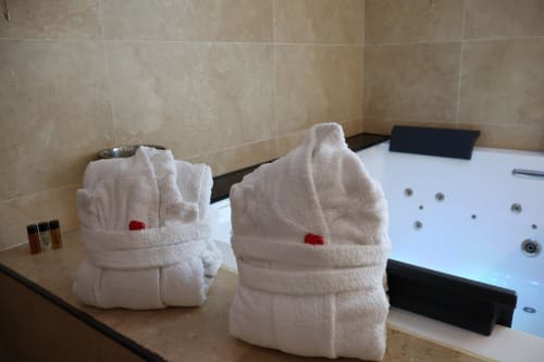 Luxury bathroom amenities at Tagasuites Catania: fluffy white towels with red accents, toiletries, and jacuzzi jets visible