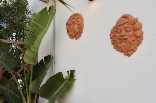 Terracotta sculptural heads on white wall beside tropical plant in Catania boutique hotel room