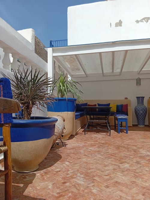Patio lumineux du riad Le Village Mogador avec jardinières bleues, coin repas et espace détente sous puits de lumière à Essaouira