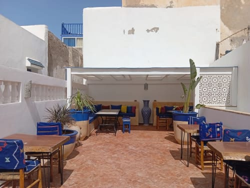 Cour ensoleillée du Riad Le Village Mogador à Essaouira avec mobilier bleu, carrelage terracotta et pergola rétractable