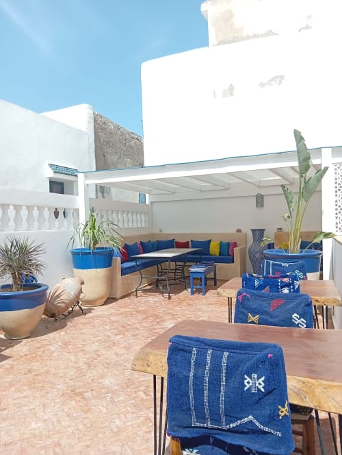 Terrasse sur le toit du Riad Le Village Mogador à Essaouira avec sièges bleus, plantes en pot et ciel dégagé