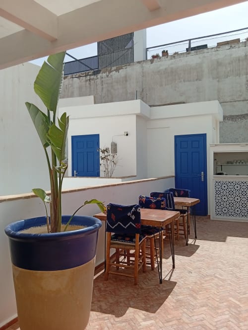 Cour du Riad Le Village Mogador avec portes bleues, sièges en bois, plante en pot et murs en béton à Essaouira