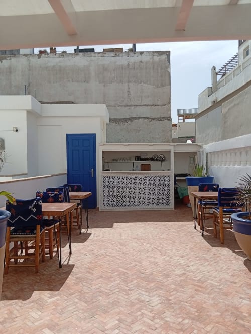 Cour intérieure du Riad Le Village Mogador à Essaouira avec tables de restaurant, porte bleue et architecture marocaine traditionnelle