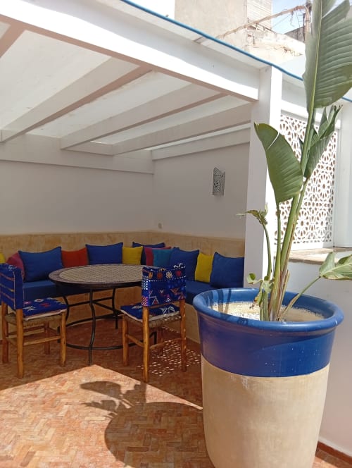 Patio traditionnel marocain à Essaouira avec sièges bleus rembourrés, table ronde, plante en pot et puits de lumière
