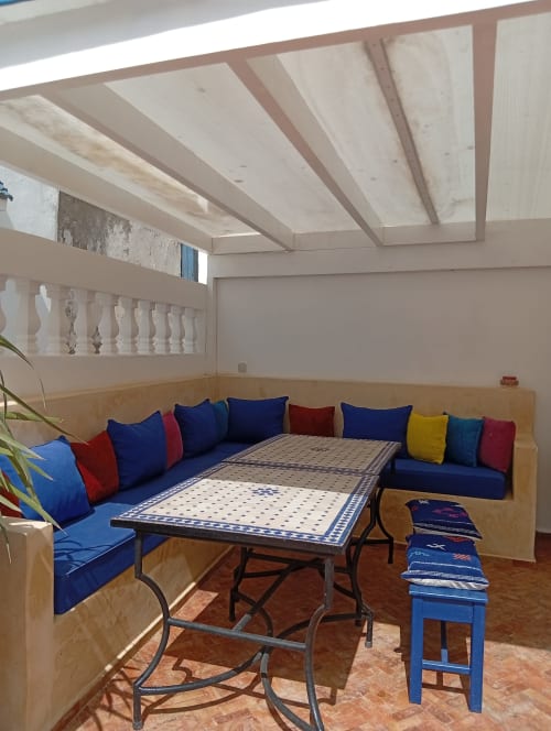 Salon traditionnel marocain du Riad Le Village Mogador avec sièges en coussins bleus, table aux motifs géométriques zellige et poutres apparentes