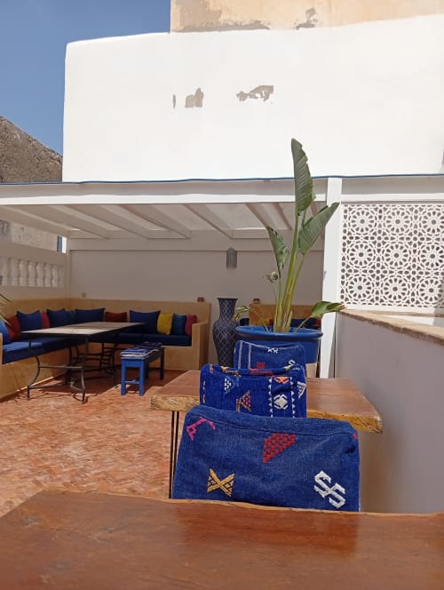 Patio du Riad Le Village Mogador avec sièges aux coussins bleus, textiles ornementaux et plante verte à Essaouira