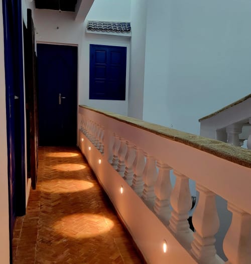 Couloir du Riad Le Village Mogador à Essaouira avec portes bleues, murs en terre cuite, sol en bois et balustrade décorée