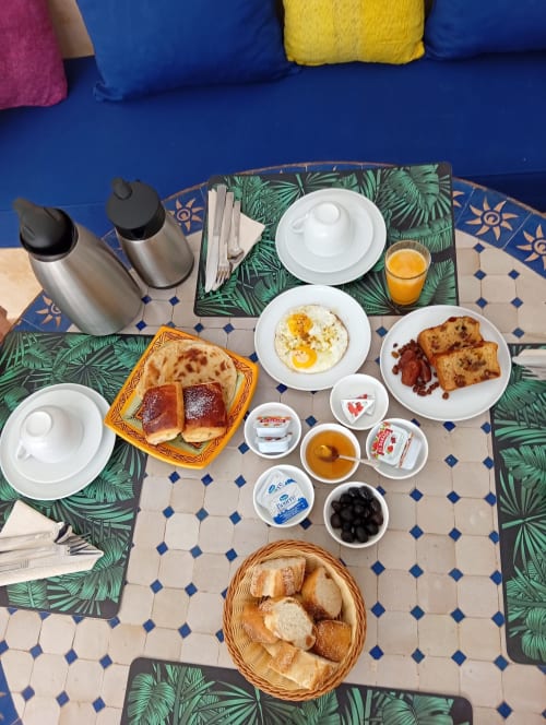 Petit-déjeuner au Riad Le Village Mogador à Essaouira avec œufs, bacon, pâtisseries, pain et jus d'orange sur carrelage bleu