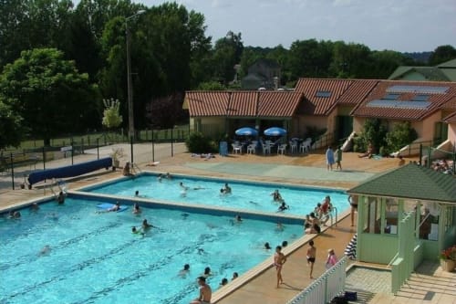 Piscine extérieure du Domaine de Châlus-Chabrol avec clients, courts de tennis en terre battue et bâtiments en terre cuite