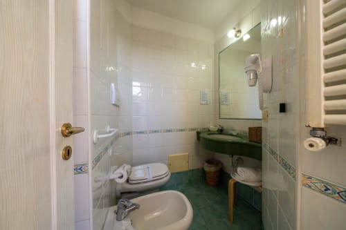 Bagno moderno della Villa Bina Sea Hotel con piastrelle bianche, lavabo verde, wc, specchio e bordatura decorativa blu