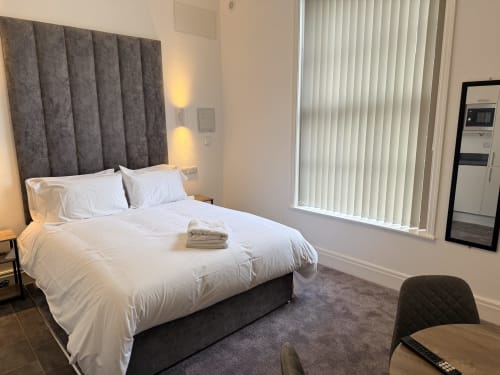 Fishergate Residences studio apartment in Preston with king size bed,, grey headboard, white linens, vertical blinds, and modern decor