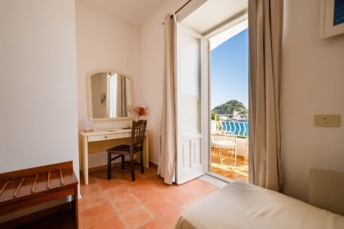 Suite con vista mare a Villa Bina Sea Hotel: scrivania con specchio, porta-finestra sulla terrazza con vista sul Mar Tirreno e il villaggio costiero