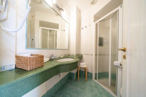 Bagno moderno della suite Villa Bina Sea Hotel con piano lavabo verde, lavabo rotondo, specchio e doccia a Serrara Fontana