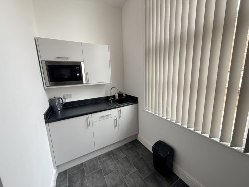 Modern kitchenette in Deluxe Studio at Fishergate Residences Preston, featuring white cabinetry, black countertop, microwave,