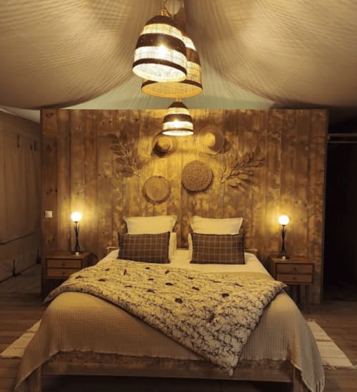 Chambre de glamping chez You & Me avec luminaires suspendus rayés, tête de lit en bois et literie confortable à Moncontour