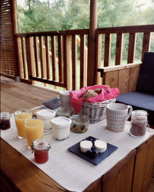 Petit-déjeuner servi sur la terrasse en bois de You & Me Glamping à Moncontour, avec jus, pâtisseries, yaourt et vue sur la forêt