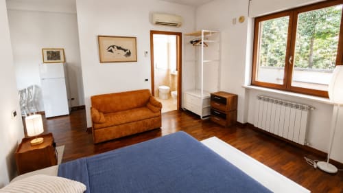 Luminoso monolocale a Roma con parquet, letto blu, divano arancione, angolo cottura e vista sul giardino