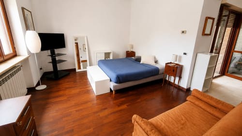 Elegante camera da letto di un appartamento romano con letto blu, pavimenti in legno, TV, divano arancione e servizi accessibili presso Myob Hotel Olgiata