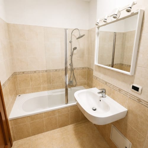 Moderno bagno nell'appartamento di Olgiata a Roma, con lavabo bianco, vasca da bagno con box doccia in vetro e scaldasalviette