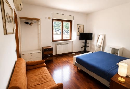 Spazioso appartamento a Roma, camera da letto con pavimento in legno, letto blu, divano marrone e vista sulla città