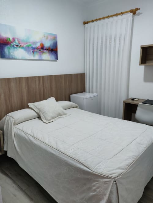 Habitación moderna del Hotel La Posada Cartagena con ropa de cama blanca, cabecera de madera, obras de arte coloridas y cortinas translúcidas.