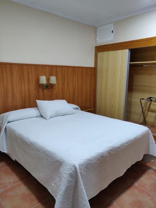 Habitación del Hotel La Posada en Cartagena con ropa de cama blanca, panelado de madera y piso de baldosa de terracota