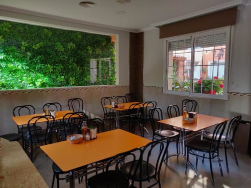 Comedor moderno del Hotel La Posada en Cartagena con mesas naranjas, sillas negras, pared verde con plantas y amplios ventanales.