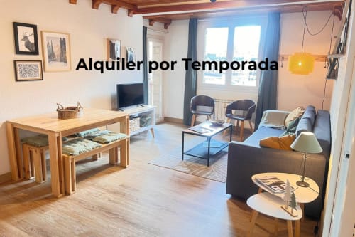 Luminoso salón en Vielha con muebles de madera, sofá, televisor y vistas a las montañas desde grandes ventanales