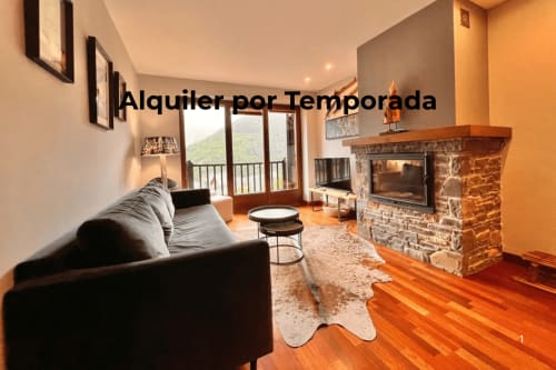 Sala de estar moderna con chimenea, sofá negro y vistas a las montañas en el alquiler Vilac