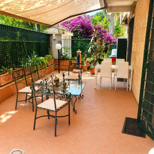 Myob apartment garden patio in Roma with dining table, chairs, vibrant magenta flowers, and shaded seating area