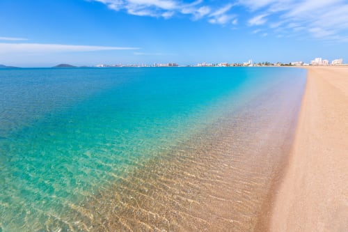 Aguas cristalinas color turquesa y playa arenosa del Hotel La Posada en Cartagena, España, con skyline de la ciudad costera