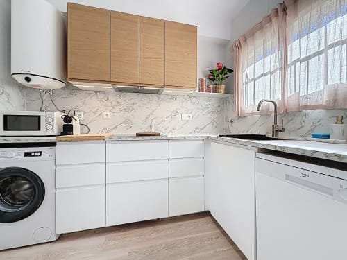 Cocina moderna de la casita La Bella Lola en Estartit con muebles blancos, encimera de mármol y armarios superiores de madera