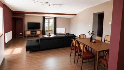 Séjour ouvert du gîte Maison Agami avec canapé noir, table en bois, téléviseur et murs bordeaux