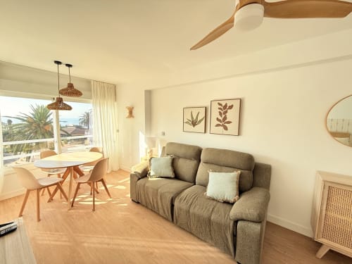 Apartamento moderno frente al mar en Algarrobo con vista al océano, sala amueblada, comedor, ventilador de techo y decoración costera.