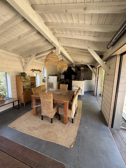 Salle à manger de la villa moderne au Domaine d'Olga avec table en bois, chaises tissées, poutres apparentes et cuisine ouverte à Aniane,