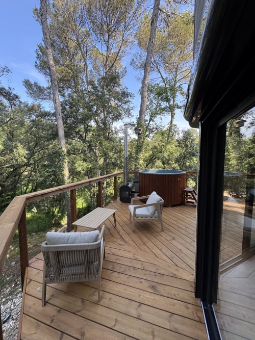 Terrasse en bois avec chaises longues et bain à remous dominant un jardin forestier à la villa Domaine d'Olga, Aniane